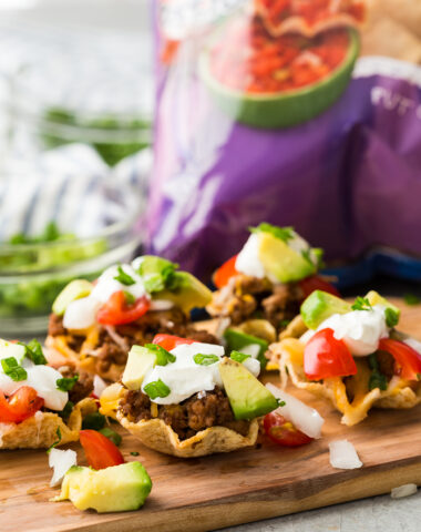 A cutting board with taco bites in Tostitos Scoops! a bag of chips in the background.