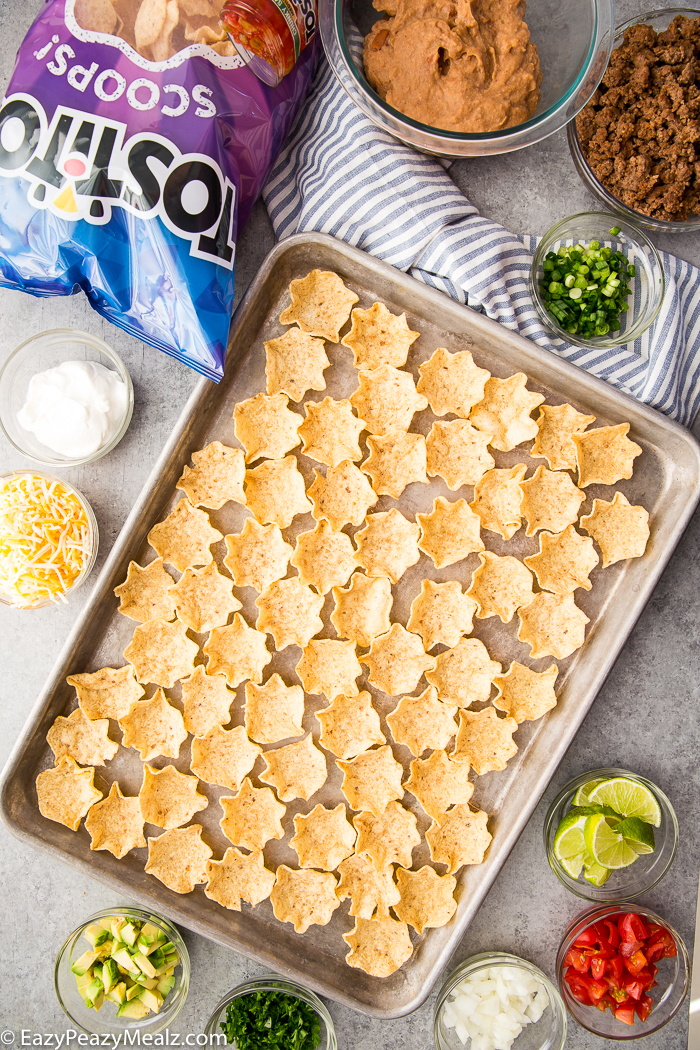 A baking tray covered in Tostitos Scoops with the fixings for taco bites around it.