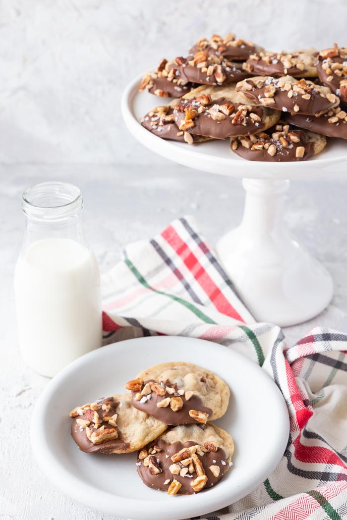 A white cake stand with cookies, as well as a plate of cookies and glass of milk