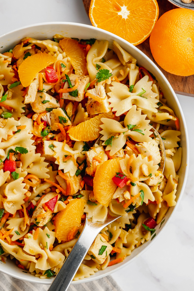 A white bowl with Asian pasta salad, oranges on the side. 