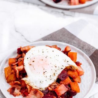 Bacon and Eggs Veggie hash on a white plate topped with an egg