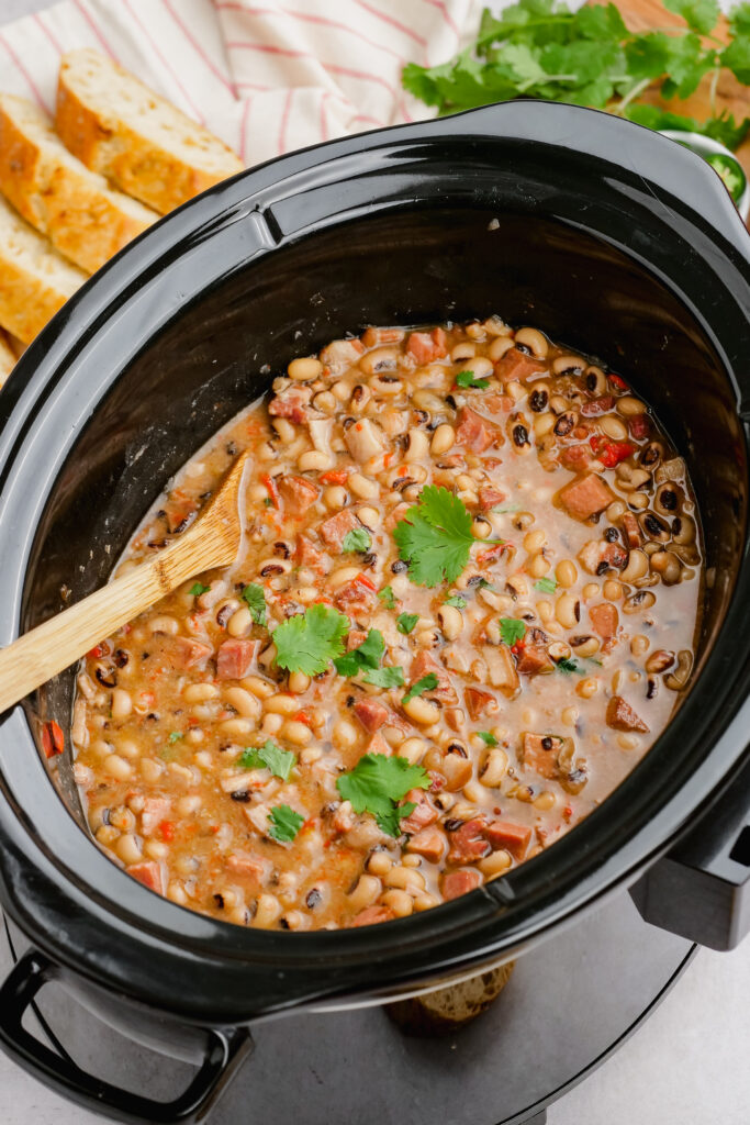 A slow cooker full of black eyed peas garnished with parsley