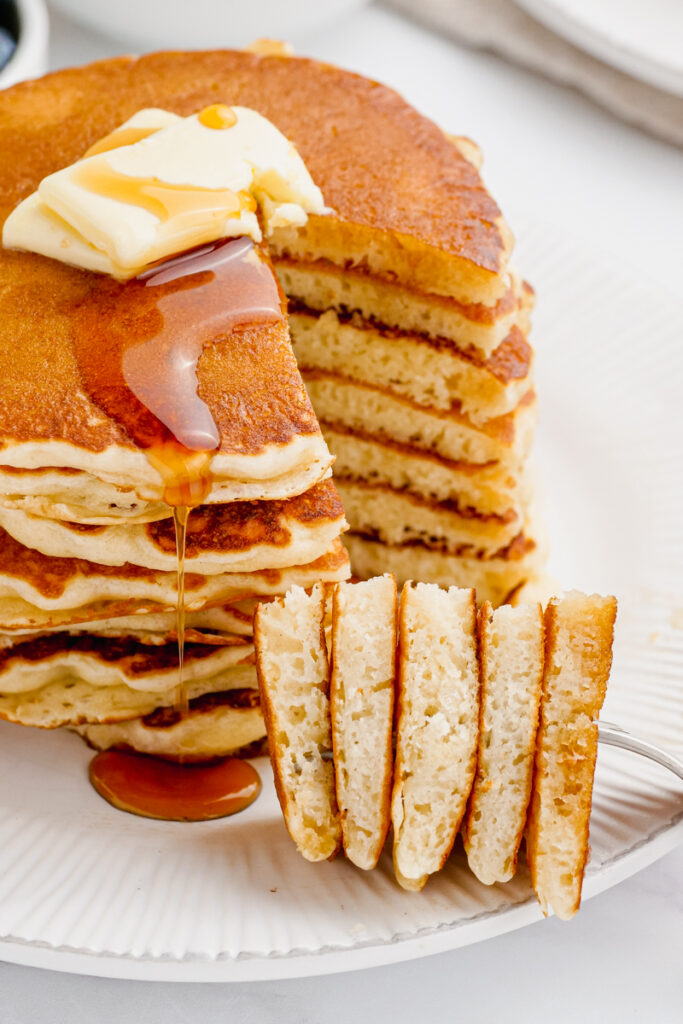 A delicious stack of buttermilk pancakes, a pat of butter on top, and a section cut out on a fork to show how fluffy they are