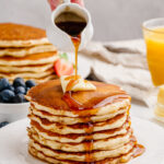 A hot stack of buttermilk pancakes and syrup being poured over the top