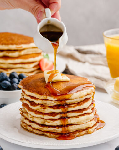 A hot stack of buttermilk pancakes and syrup being poured over the top