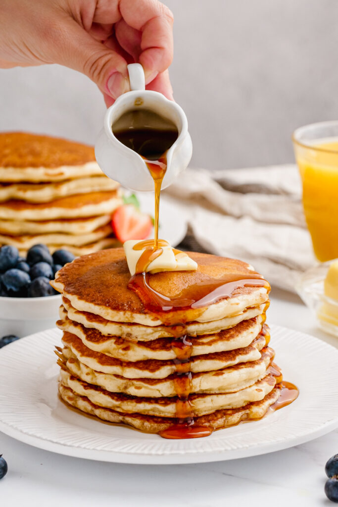 A hot stack of buttermilk pancakes and syrup being poured over the top