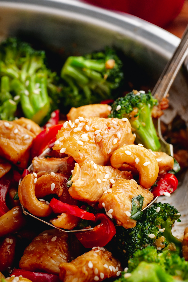 A stainless steel pan full of cashew chicken with a spoon ful elevated partially out of the pan.