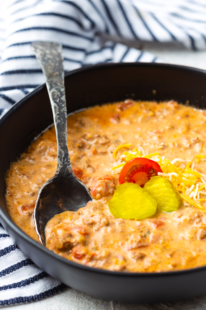 Cheeseburger soup, cheesy, beefy soup in a black bowl, garnished with pickles and tomatoes, and cooked in the slow cooker