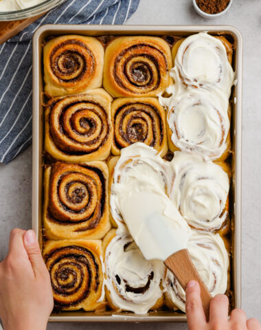 The best gooey, delicious, cinnamon rolls, top down shot, spreading cream cheese icing over the top.