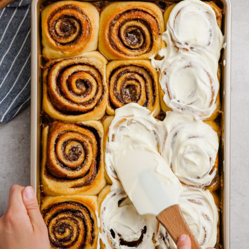 The best gooey, delicious, cinnamon rolls, top down shot, spreading cream cheese icing over the top.