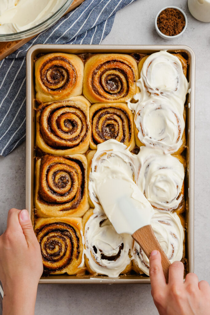 The best gooey, delicious, cinnamon rolls, top down shot, spreading cream cheese icing over the top. 