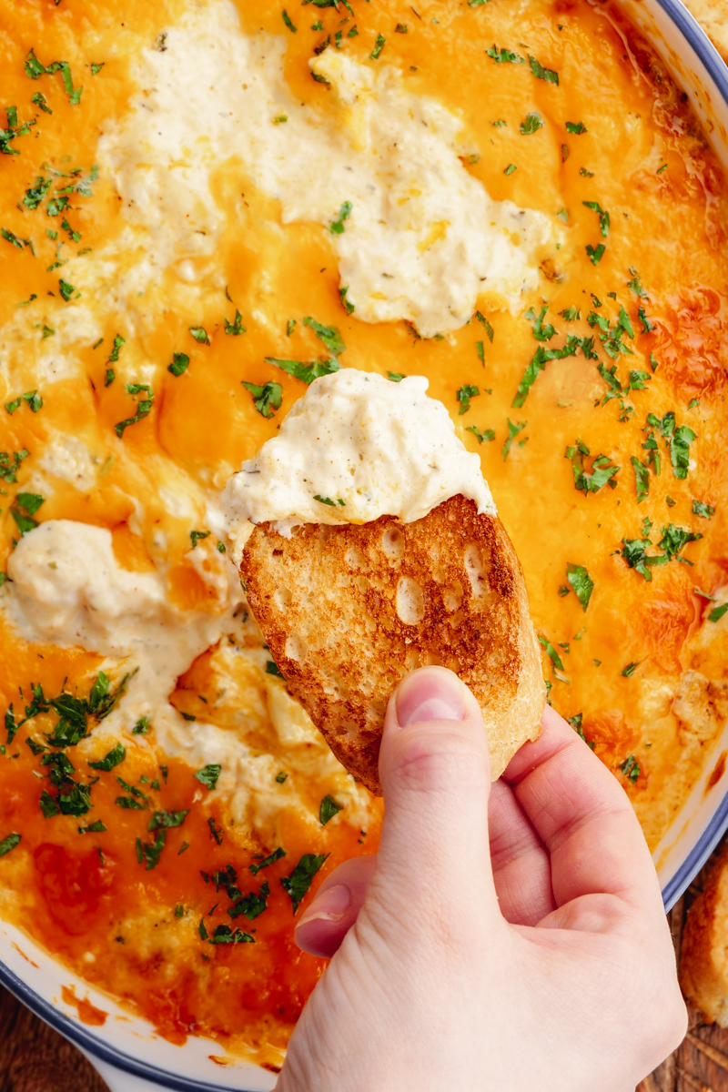 A casserole dish of crab dip, topped with cheese, and bread dippers. 