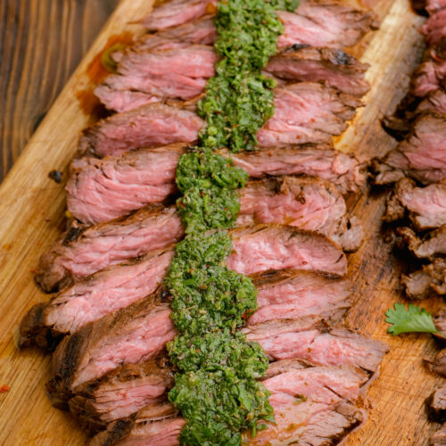 Grilled skirt steak on a cutting board with chimichurri on top