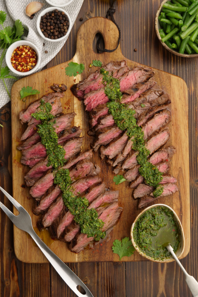 Grilled skirt steak on a cutting board, and topped with chimichurri