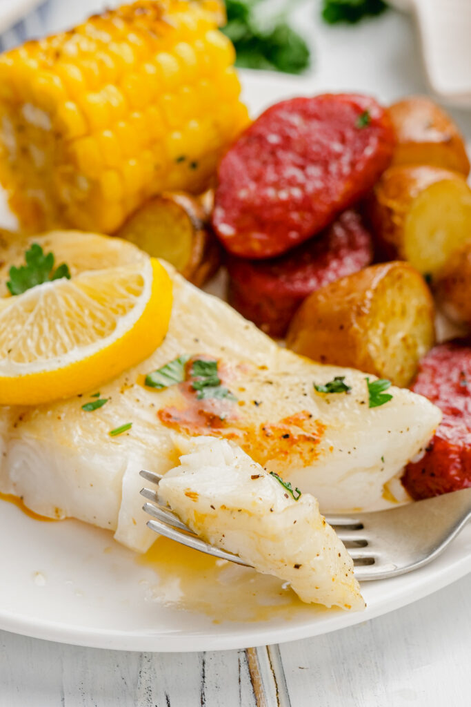 Roasted Halibut Sheet Pan Dinner on white plate with fork into a piece.