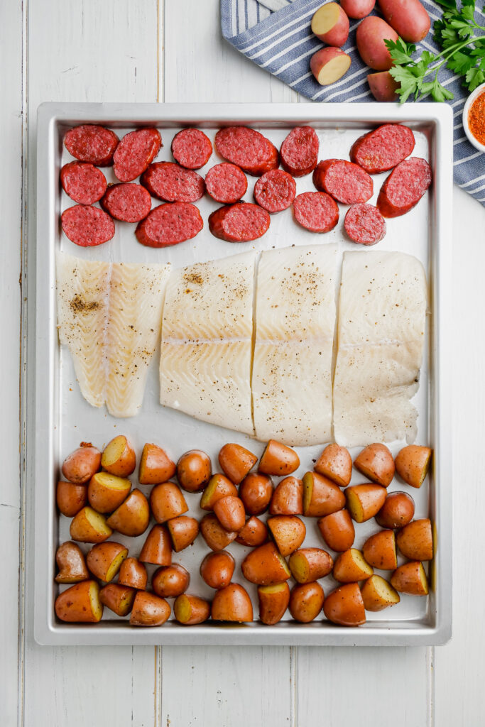 Seasoned halibut on a sheet pan with sausage and potatoes to cook