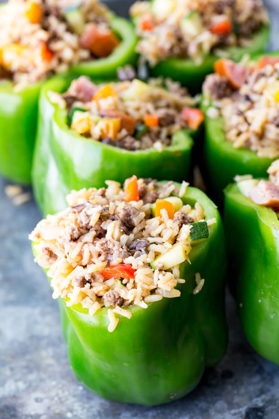 Green bell peppers stuffed with rice, sausage, and vegetables ready to be baked or frozen, sitting on a gray table