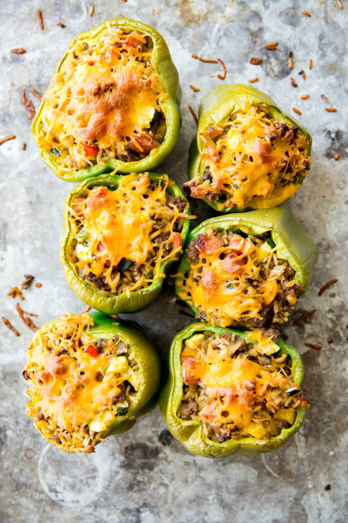 Stuffed green bell peppers topped with cheese on a gray stone table 