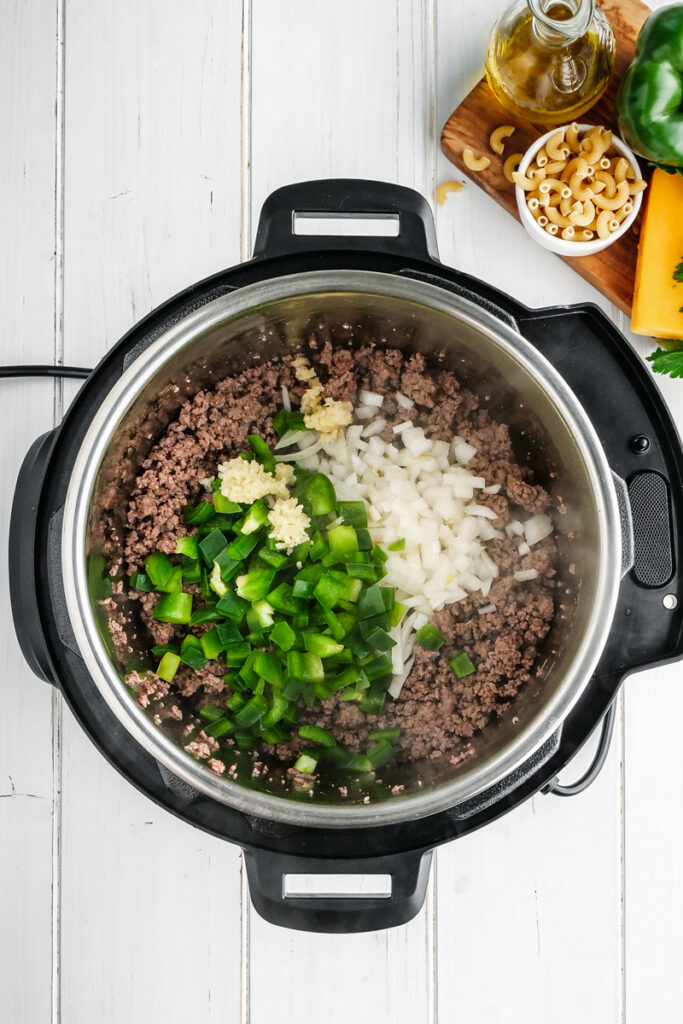 An instant pot with ground beef, onions, peppers, and minced garlic. 