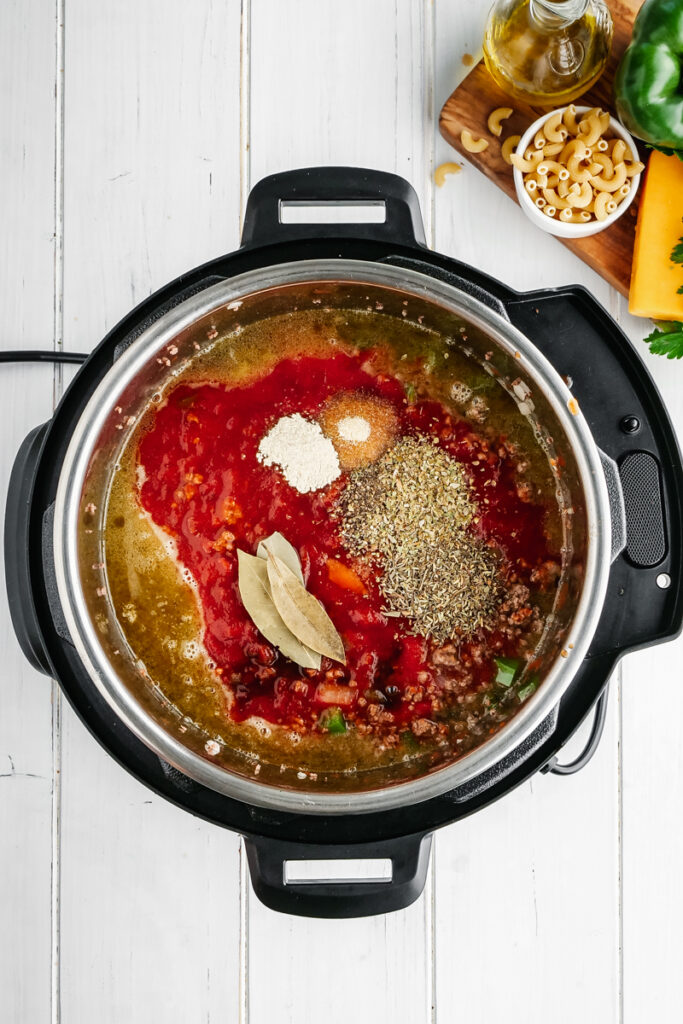 An instant pot with the beginnings of American Goulash, spices, ground beef, onions, and peppers