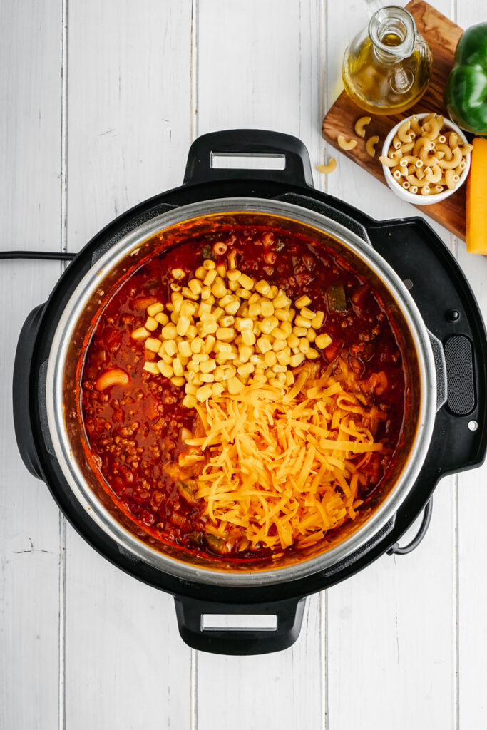 An instant pot with tomato sauce, corn, cheese, and macaroni, to make American Goulash. 