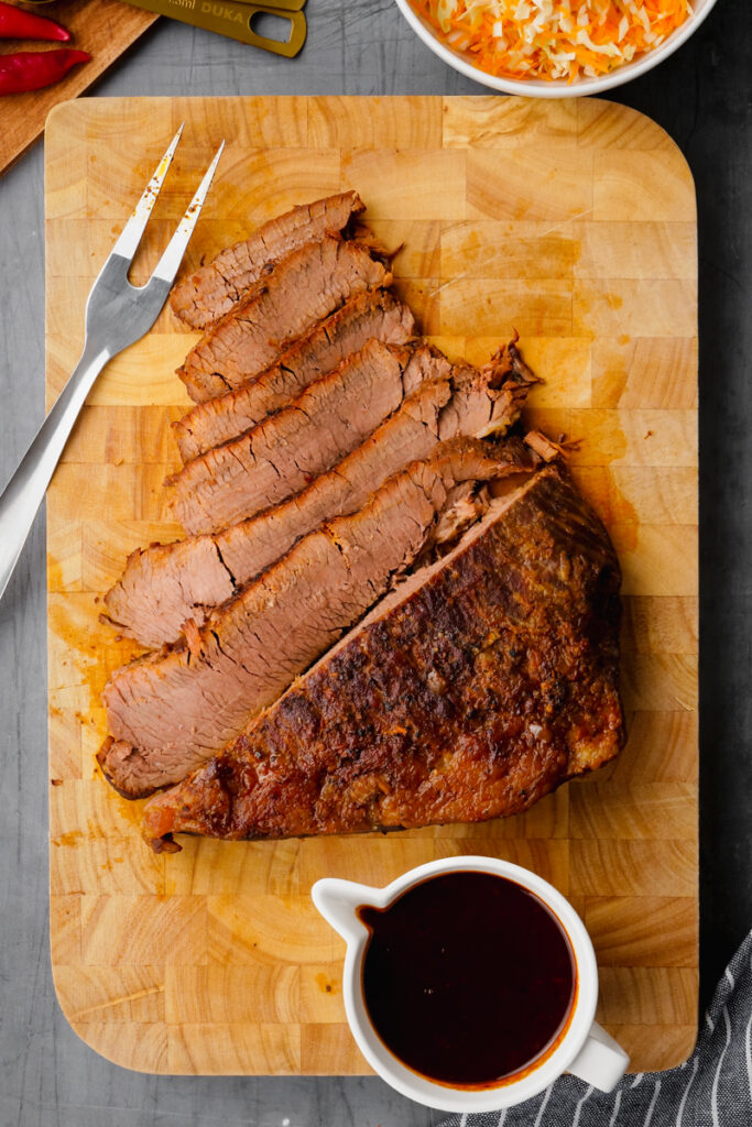 instant pot brisket on cutting board with sauce to the side