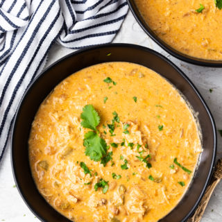 two bowls of instant pot white chicken chili, bowls are black, striped napkin in corder, soup garnished with cilantro leaves