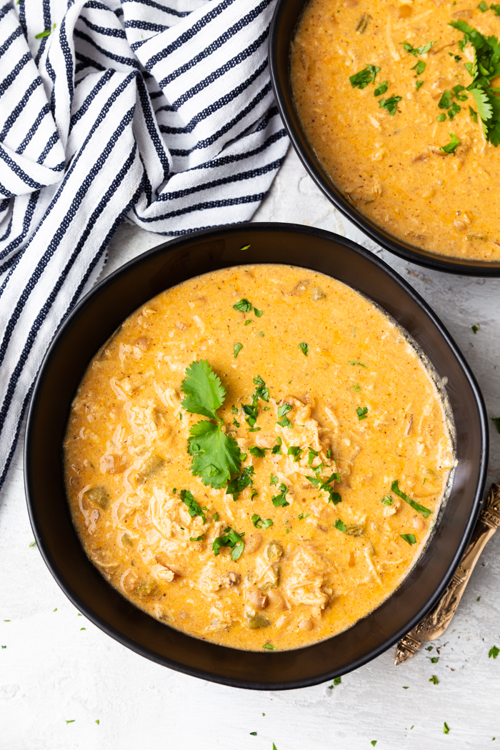 two bowls of instant pot white chicken chili, bowls are black, striped napkin in corder, soup garnished with cilantro leaves