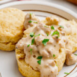 A white plate with sausage gravy over biscuits on it.