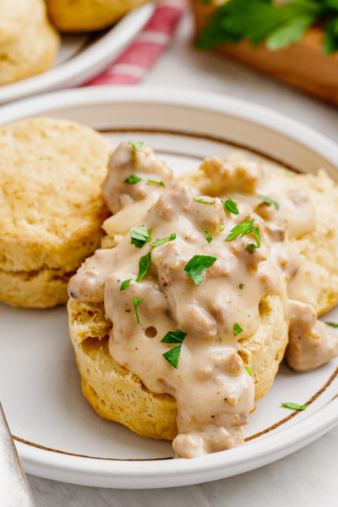 A white plate with sausage gravy over biscuits on it.