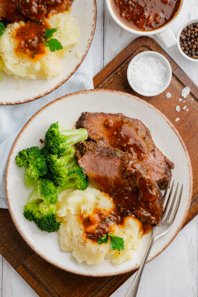Instant Pot Sirloin Roast Beef with Mushroom Sauce on a white plate with a fork, broccoli and ashes potatoes to the side.
