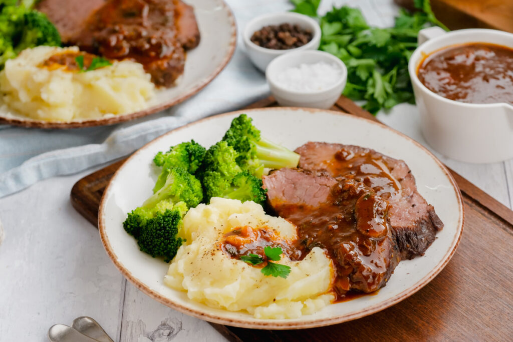 Instant Pot Sirloin Roast Beef with Mushroom Sauce on a white plate with broccoli and mashed potatoes to the side.