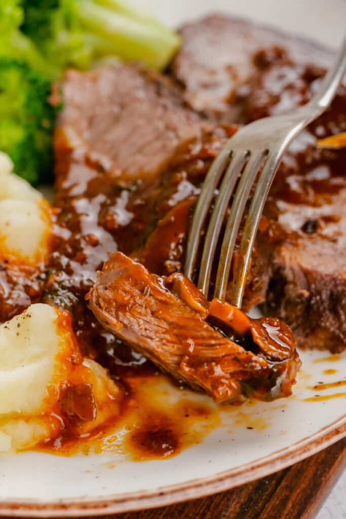 this delicious Instant Pot Sirloin Roast Beef with Mushroom Sauce on a white plate with fork into it with broccoli and mashed potatoes to the side.