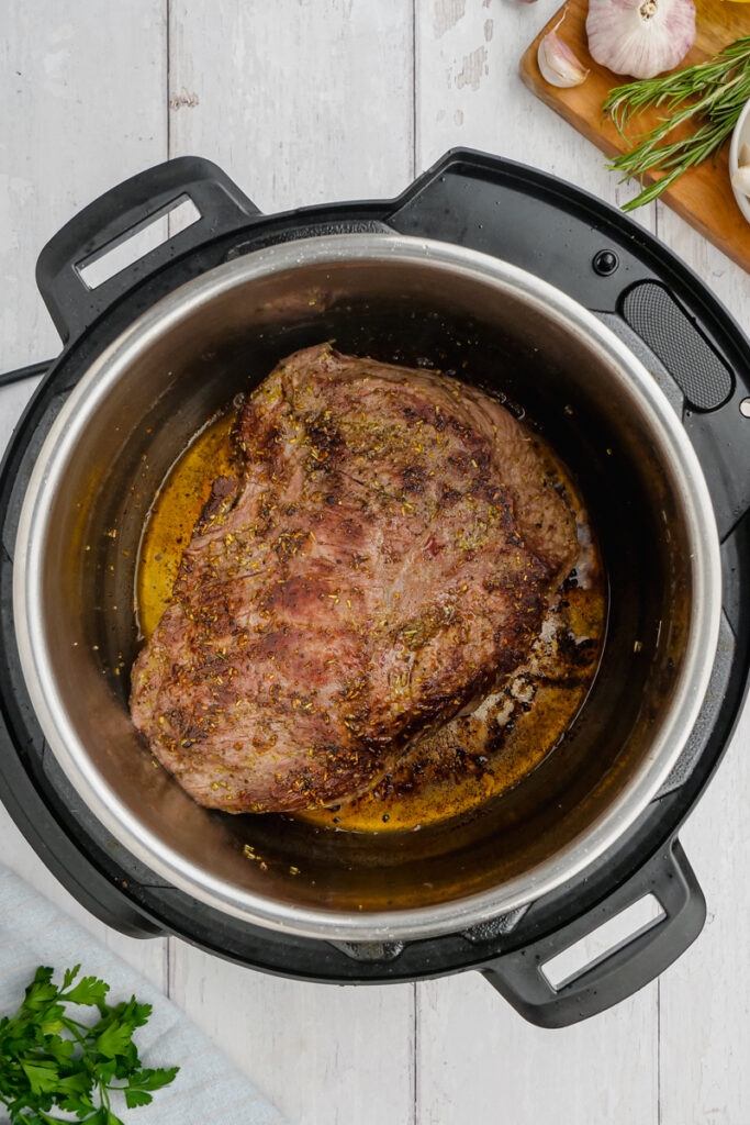 Instant Pot Sirloin Roast Beef with Mushroom Sauce in the instant pot with basil to the side.