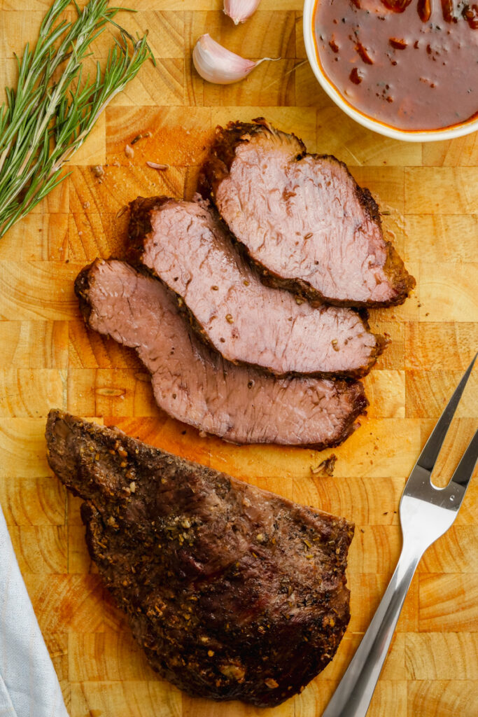 Instant Pot Sirloin Roast Beef with Mushroom Sauce on a cutting board with basil to the side