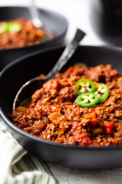 a black bowl full of keto chili, topped with jalapenos. This low carb chili has a spoon in it.