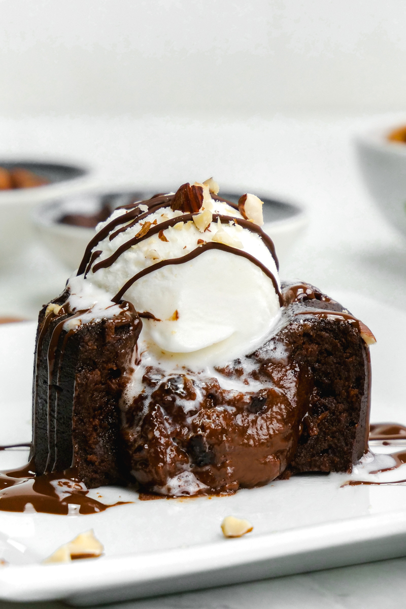 Nutella molten lava cake with center oozing out, on a white plate. Molten lava cake is topped with ice cram