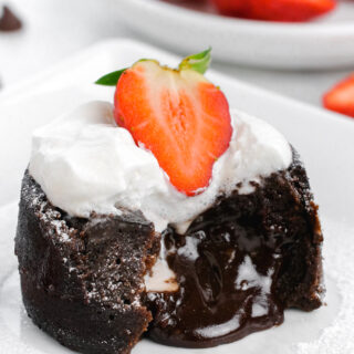 Chocolate molten lava cake, with the lava coming out the front, topped with whipped cream and strawberries