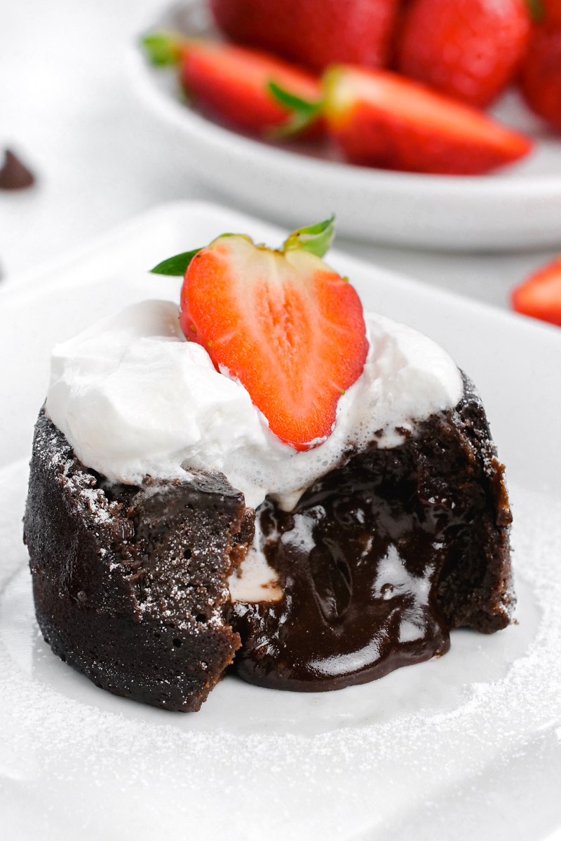 Chocolate molten lava cake, with the lava coming out the front, topped with whipped cream and strawberries