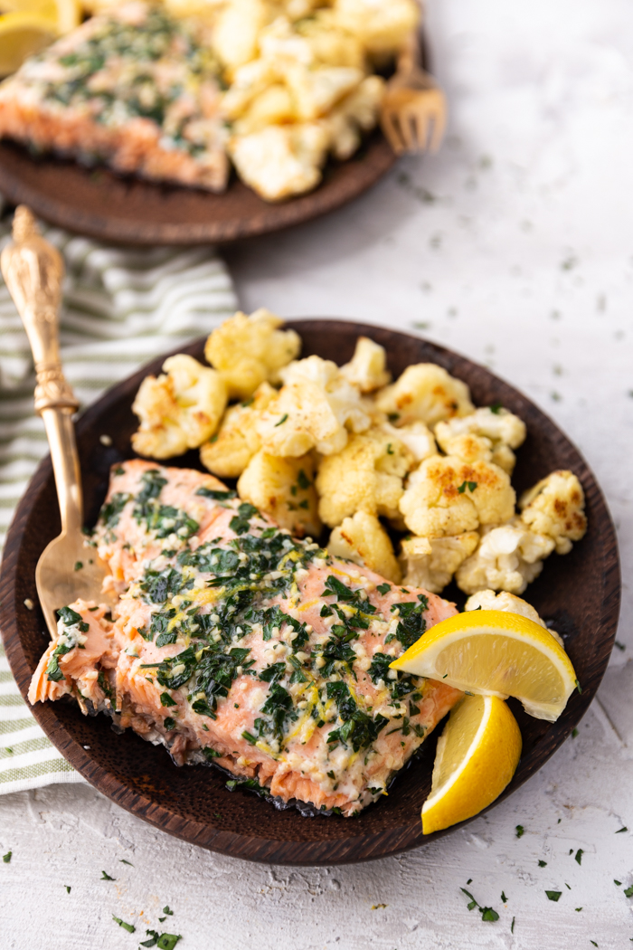 lemon parsley garlic salmon with cauliflower on a wooden plate with lemon wedges