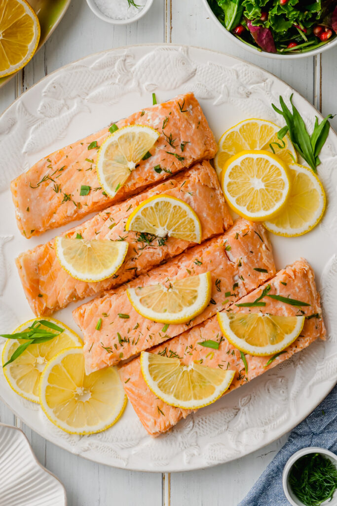 A white plate with oven poached salmon and lemons and dill