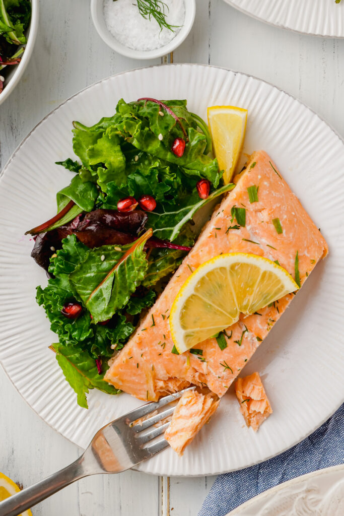 A white plate with oven poached salmon and lemon slices