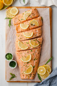 Oven poached salmon filet on a cutting board with lemons and dill