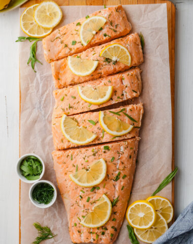 Oven poached salmon filet on a cutting board with lemons and dill