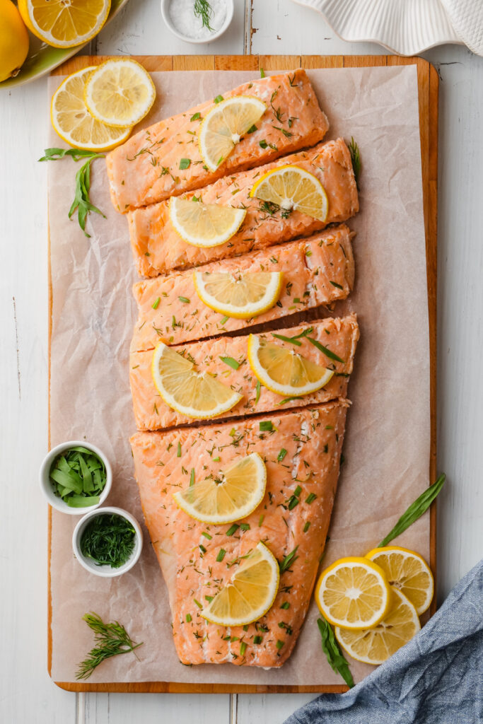 Oven poached salmon filet on a cutting board with lemons and dill