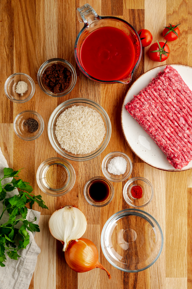 Ingredients for porcupine meatballs in little glass bowls, with ground beef on a white plate
