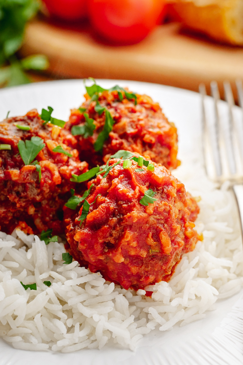 Porcupine meatballs on a bed of rice, on a white plate, fork on the side. 