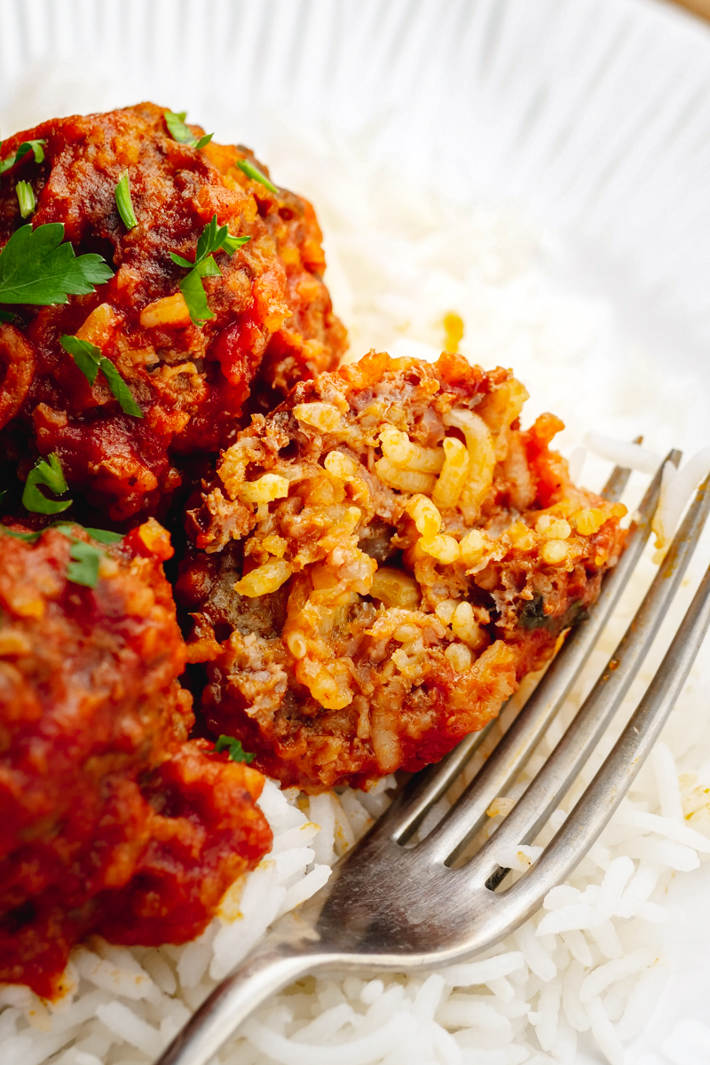 Porcupine meatballs, rice and sauce with a homemade meatball, and fork on the side. 