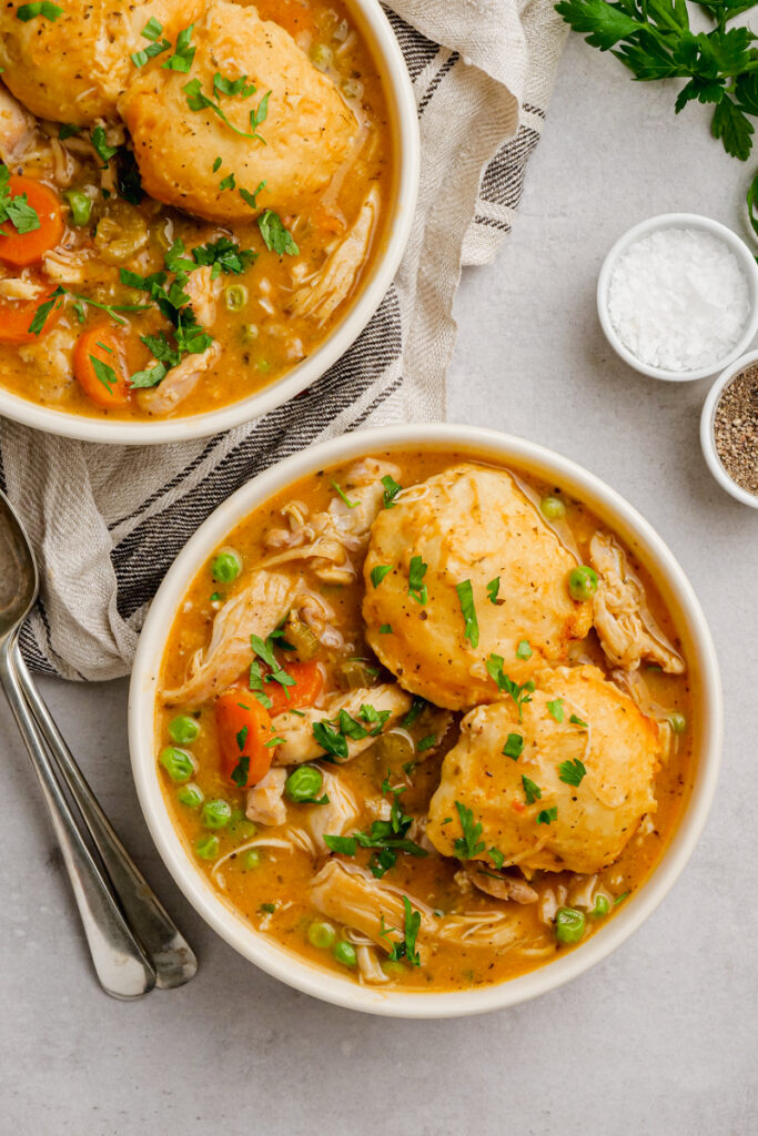 Slow cooker chicken and dumplings in a white bowl with silverware on the side