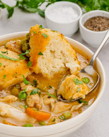 Slow cooker chicken and dumplings in a white bowl with a spoon in it, salt and pepper and parsley in the background